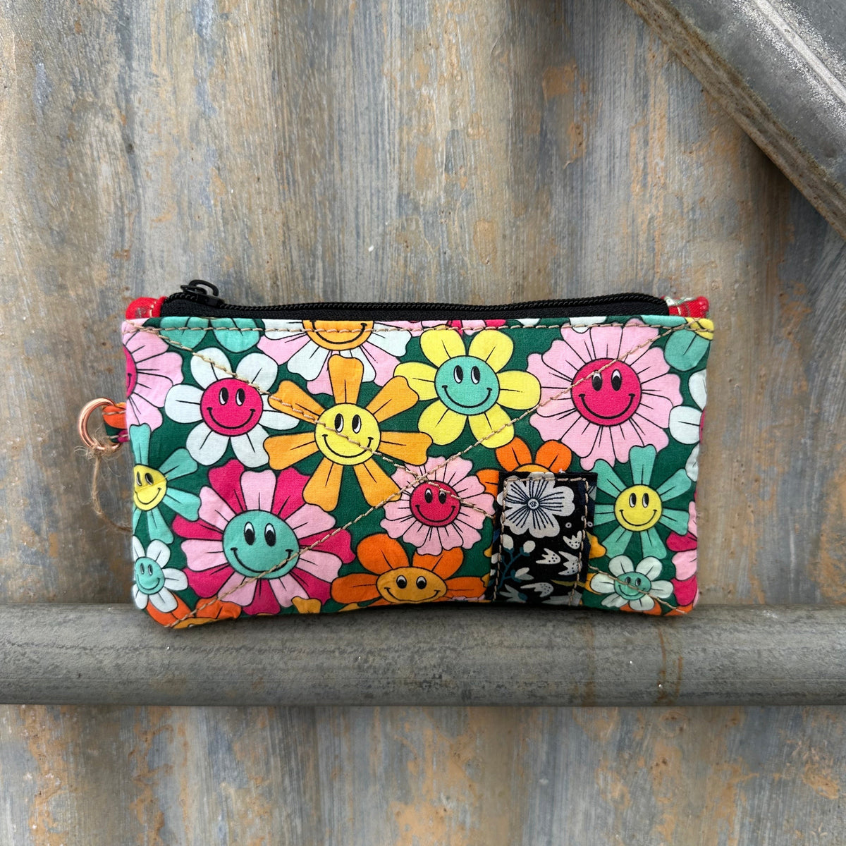 A small rectangular zip pouch with a colourful smiley-face flower print