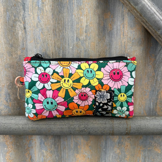 A small rectangular zip pouch with a colourful smiley-face flower print